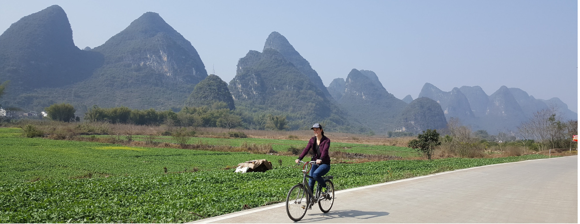 Boise travel agent, Jennifer, riding a bicycle in front of a karst mountain range in China.